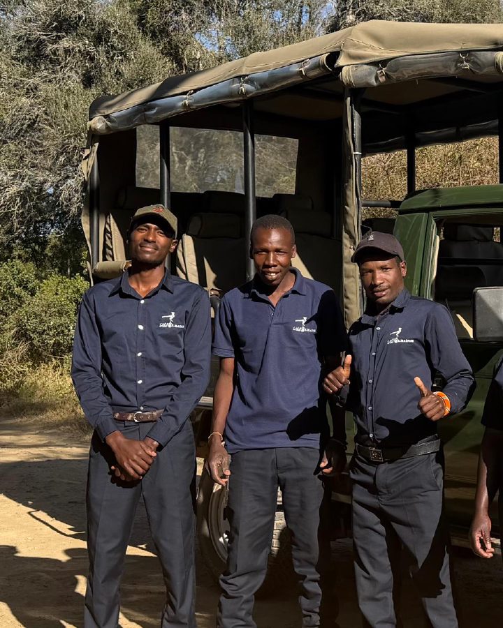 Mwangi standing with the Ol Maisor team beside a safari vehicle.