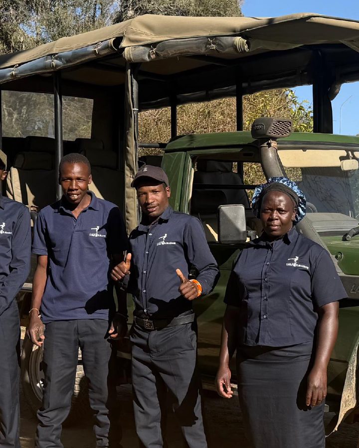 Mwangi standing with the Ol Maisor team beside a safari vehicle.